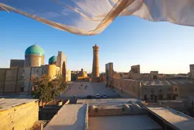Ein wehender Schal rahmt den Blick auf das Kalon-Minarett und die türkisen Kuppeln der Mir-i-Arab-Madrasa in Buchara.