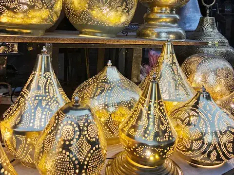 Nahaufnahme von kunstvoll gefertigten, goldenen Lampen mit filigranen Lochmustern, die auf einem Basar in Kairo leuchten.