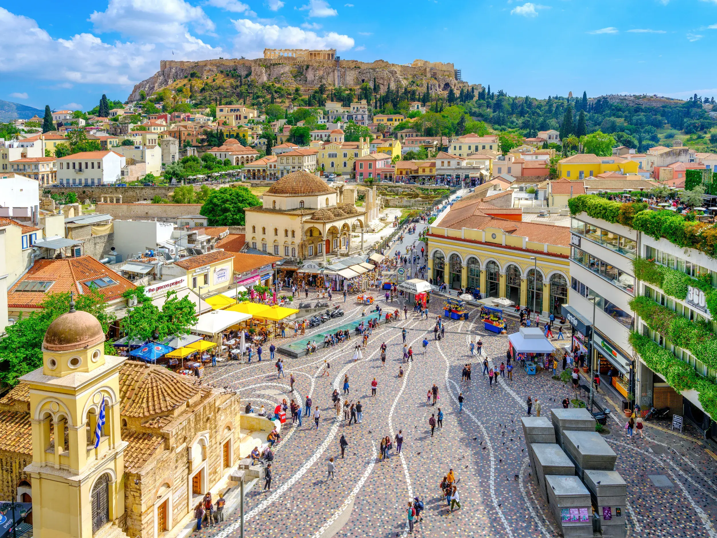 Pulsierendes Leben auf dem Monastirakiplatz in Athen mit Blick auf das historische Häusermeer und die majestätische Akropolis.