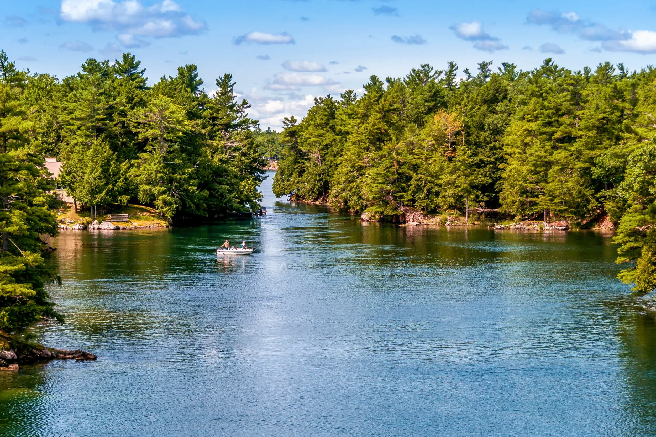 Kleines Motorboot auf dem Sankt-Lorenz-Strom in der weiten Inselwelt der Thousand Islands bei sonnigem Wetter in Kanada.