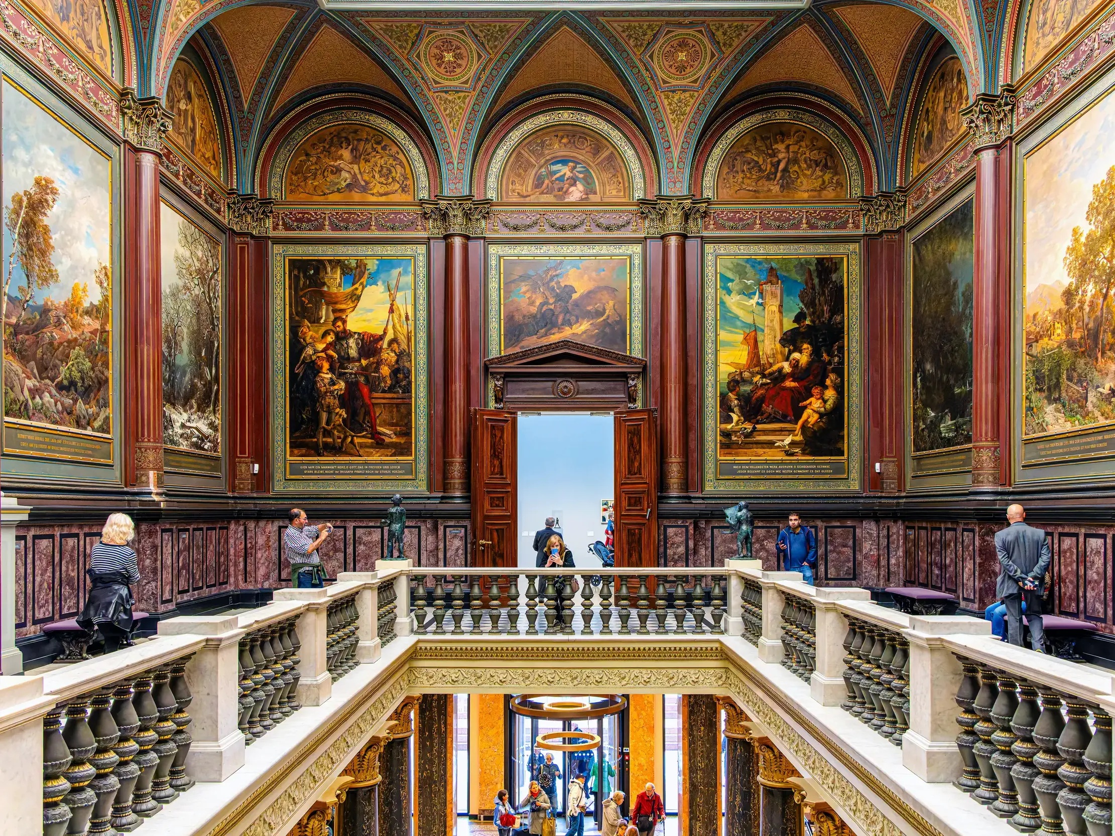 Besucher im prunkvollen Treppenhaus der Hamburger Kunsthalle mit historischen Gemälden und Bögen.