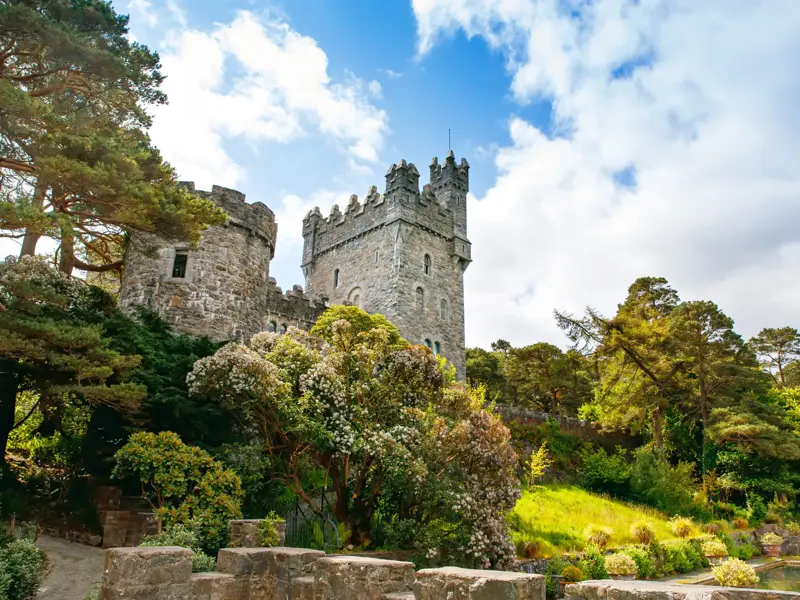 Das malerische Glenveagh Castle im Glenveagh Nationalpark in Irland, umgeben von grünen Gärten bei Sonnenschein.