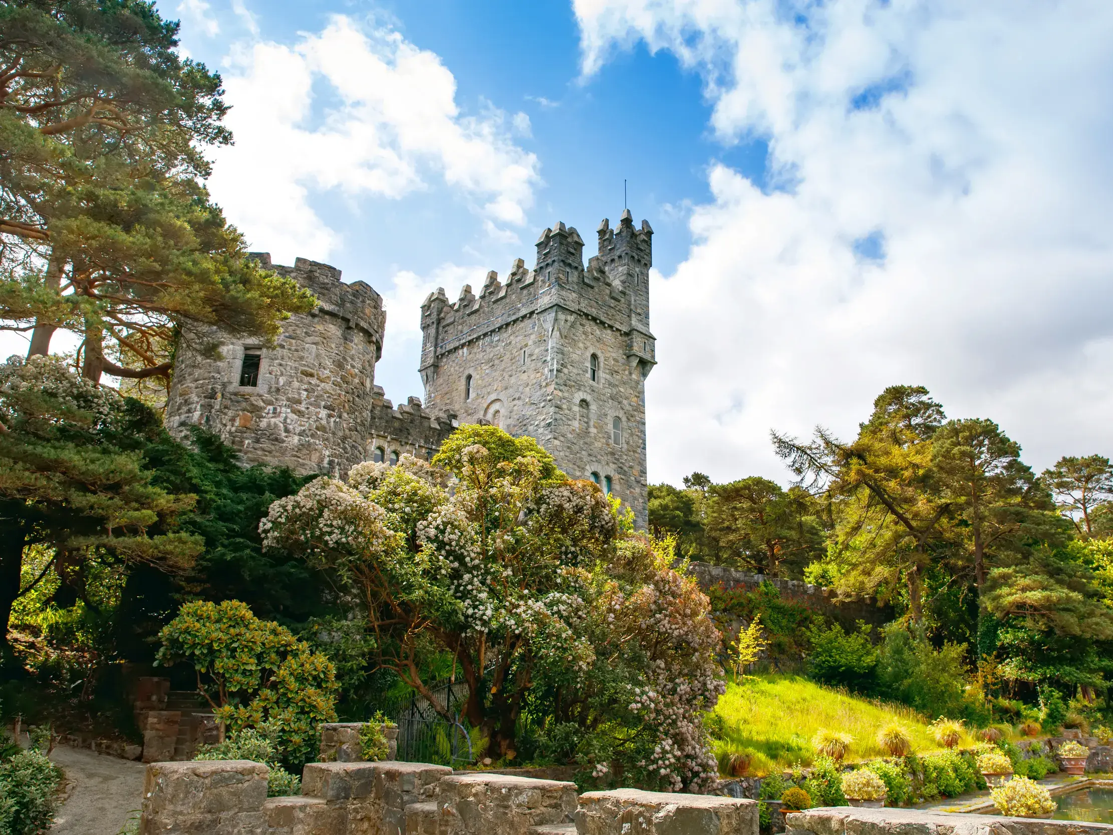 Das steinerne Glenveagh-Schloss inmitten der grünen Parkanlage des Glenveagh Nationalparks in Irland unter blauem Himmel.