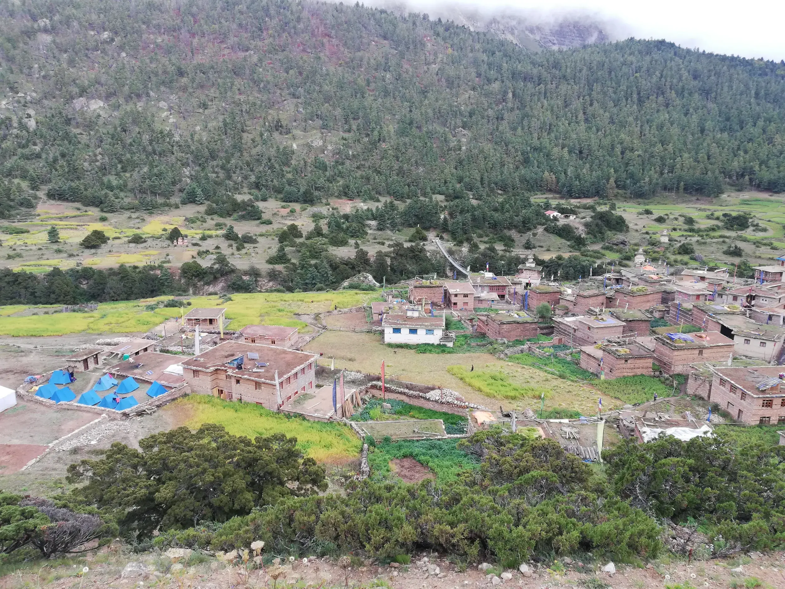 Blick von oben auf das Dorf Dho Tarap im Dolpo-Tal mit traditionellen Steinhäusern und dem blauen Zeltlager der Hauser-Gruppe.