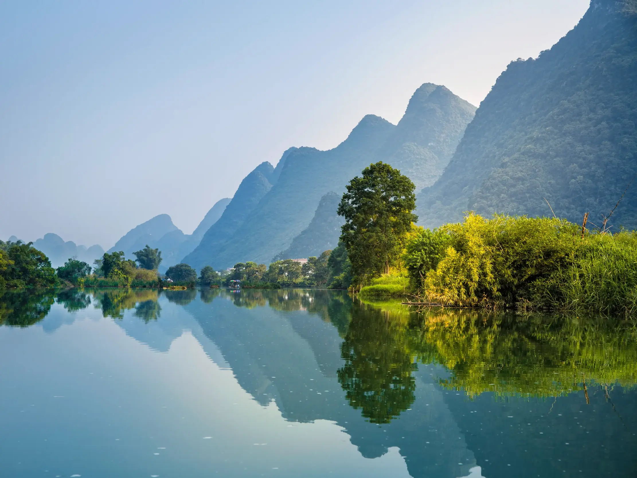 Ruhige Flusslandschaft am Li-Fluss in Yangshuo. Üppig grüne Ufer und die berühmten Zuckerhutberge spiegeln sich im Wasser.