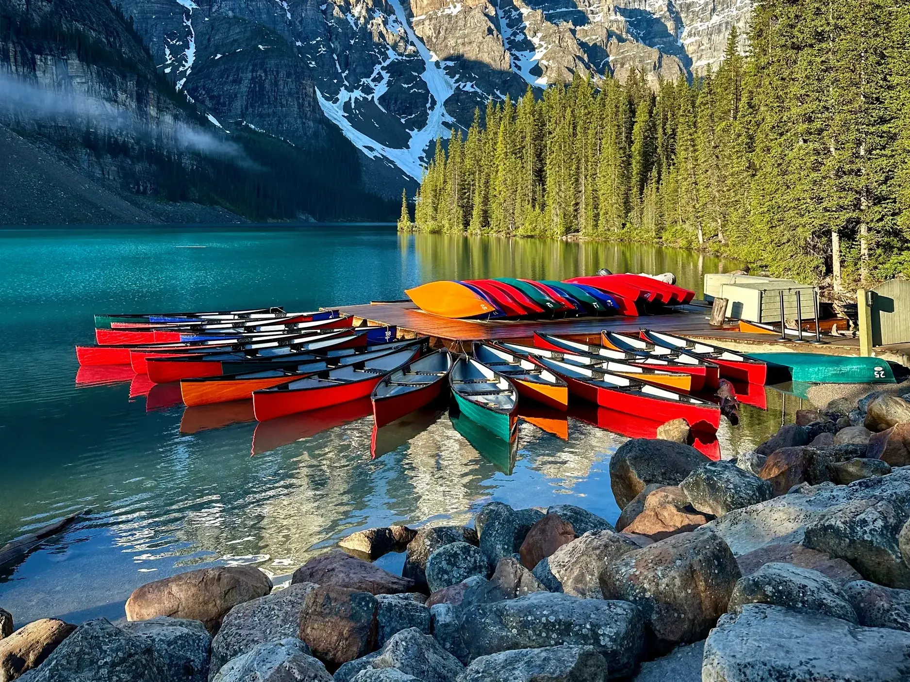 Bunte Kanus an einem Steg auf dem türkisen Moraine Lake mit den Rocky Mountains im Banff-Nationalpark im Hintergrund.