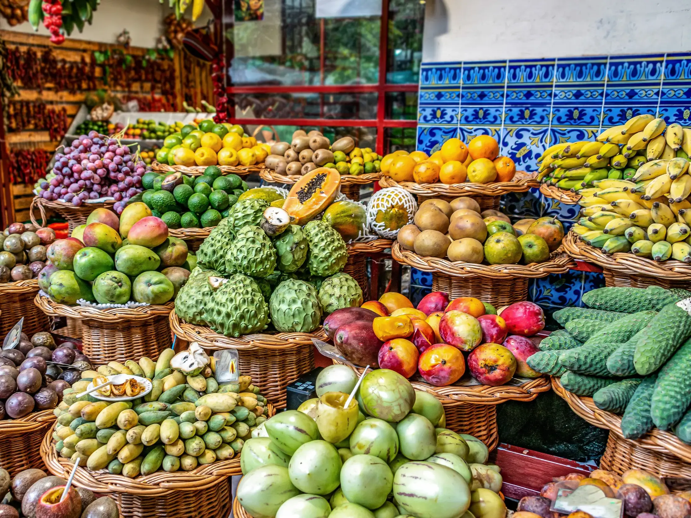 Farbenfrohe Auslage exotischer Früchte in Weidenkörben in der Markthalle von Funchal auf einer Wanderreise auf Madeira.