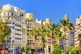 Historische Prachtbauten in der Altstadt von Valencia, gesäumt von Palmen und einem Brunnen unter strahlend blauem Himmel.