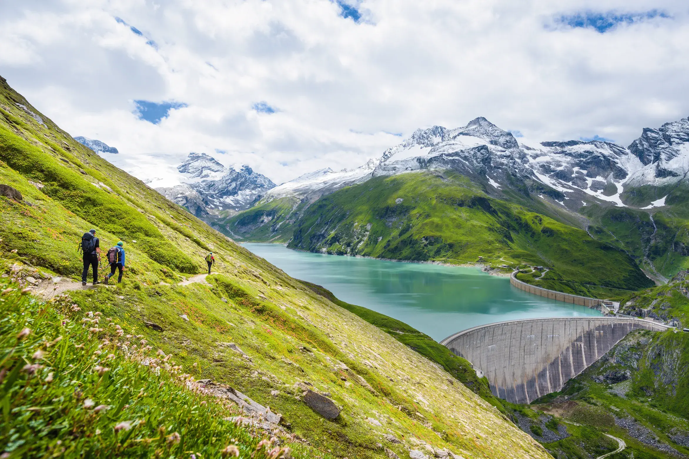Eine Wandergruppe auf einem Pfad oberhalb des türkisblauen Mooserboden-Stausees im Nationalpark Hohe Tauern.