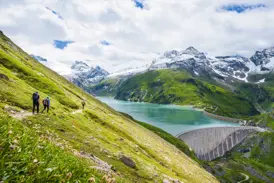 Eine Wandergruppe auf einem Pfad oberhalb des türkisblauen Mooserboden-Stausees im Nationalpark Hohe Tauern.