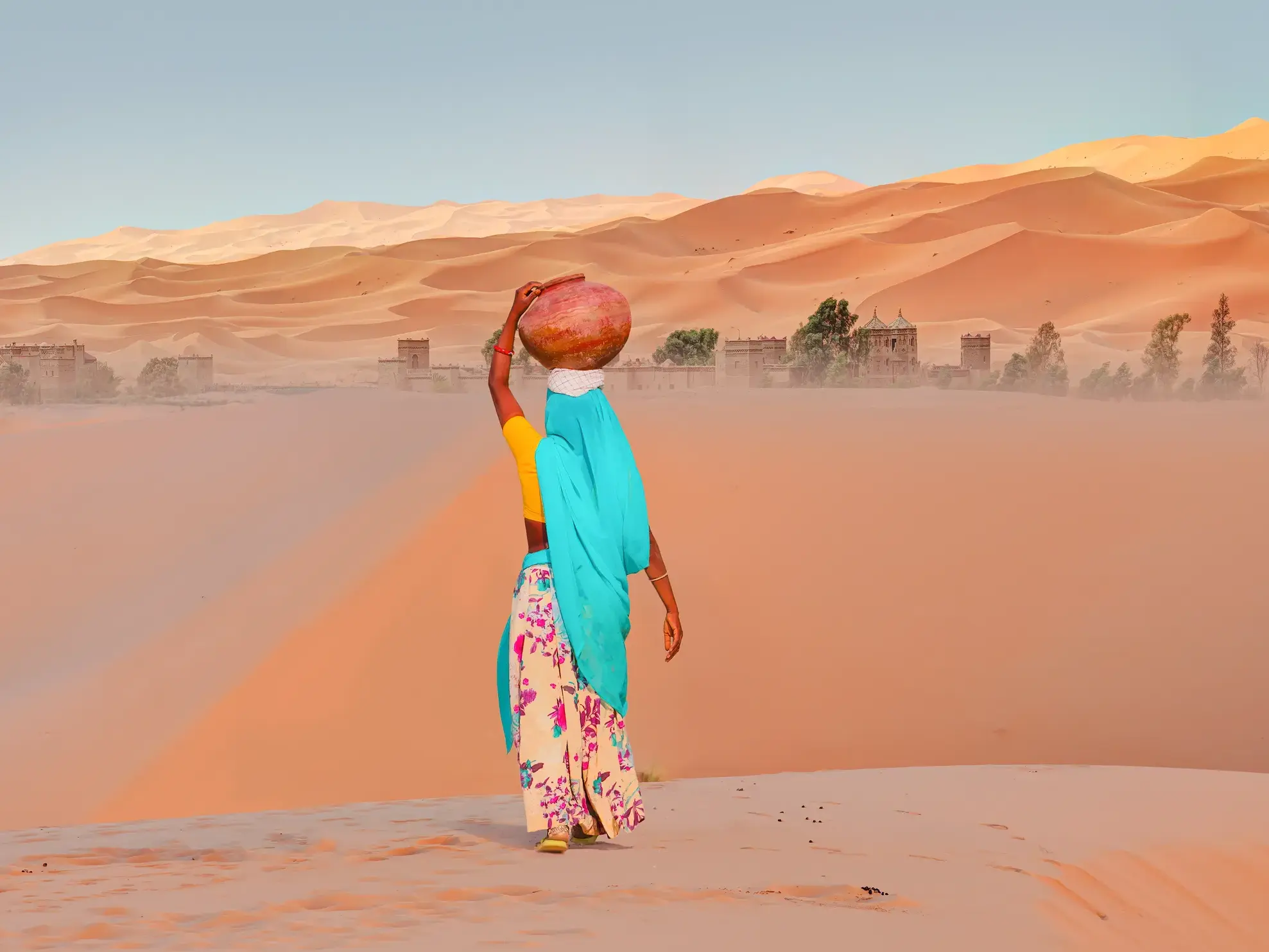 Frau mit Tonkrug auf dem Kopf wandert durch die weite Wüstenlandschaft der Sanddünen des Erg Chebbi.