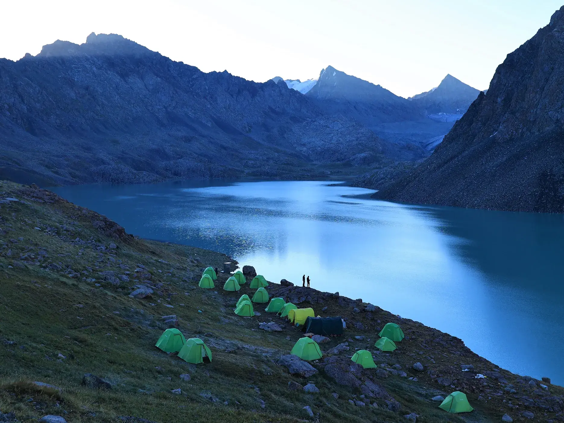 Grüne Zelte des Trekking-Camps am Ufer des türkisen Alaköl Sees vor der Bergkulisse des Terskej-Alatau in Kirgistan.