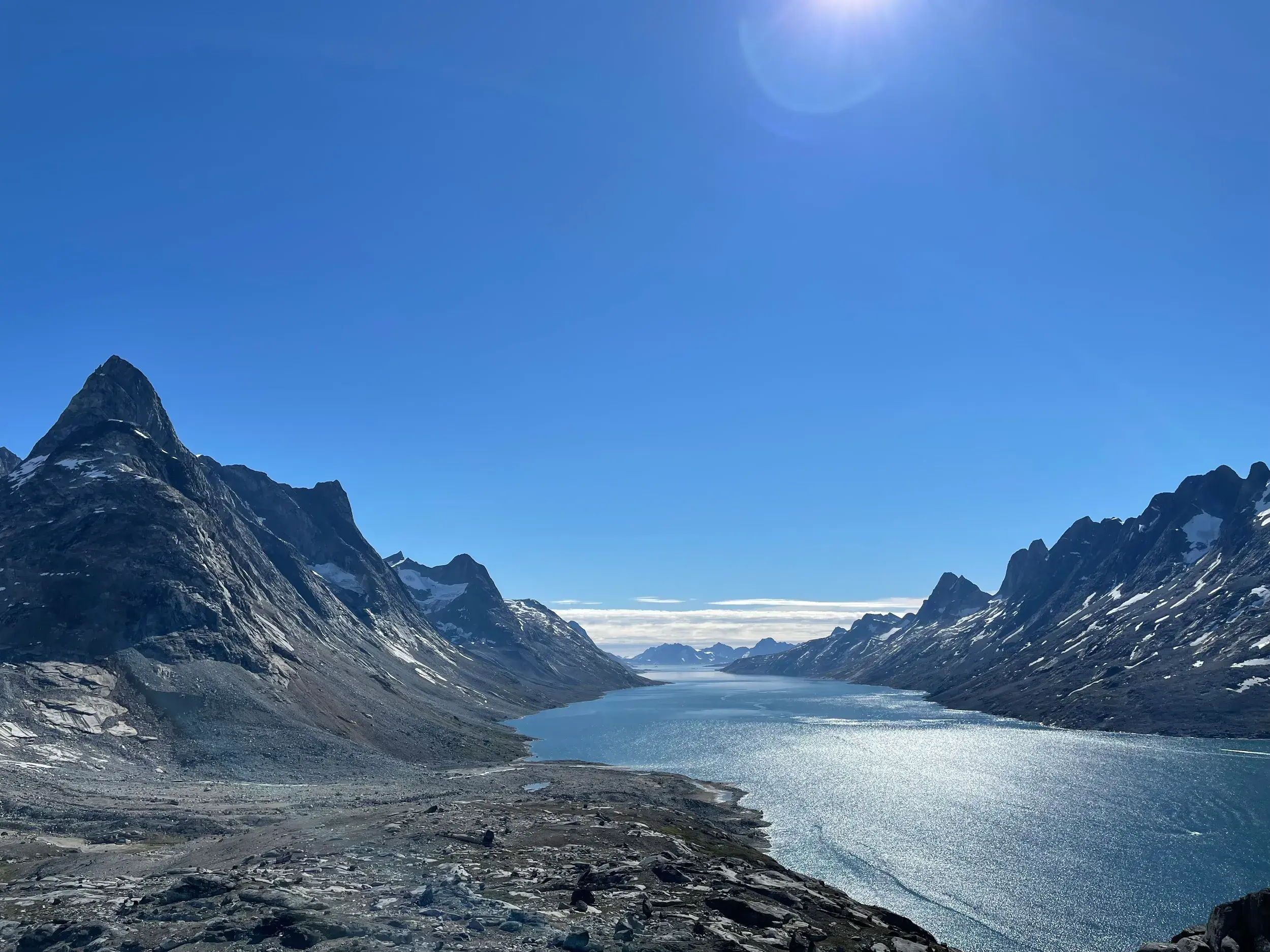 Erhabener Ausblick auf einen von spitzen Felsgipfeln gesäumten Fjord während einer Trekkingtour in der Arktis Ostgrönlands.