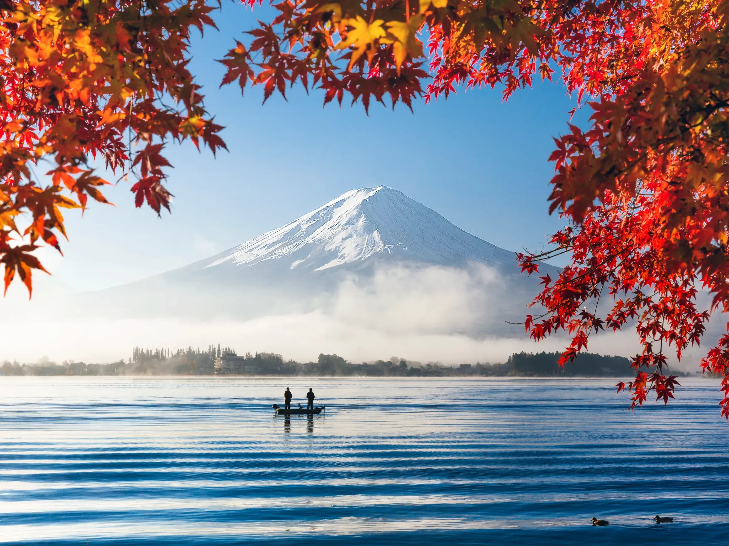 Zwei Personen in einem Boot auf einem See im Fuji-Hakone-Nationalpark mit Blick auf den schneebedeckten Fuji-san im Herbstlaub.