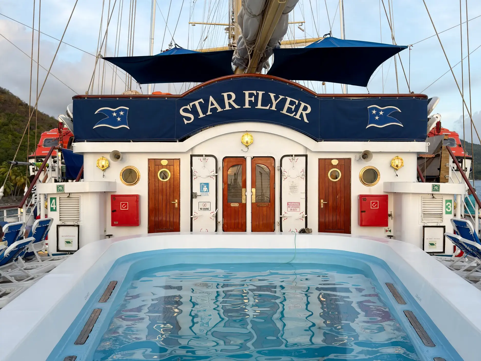 Blick vom Deck über den Pool auf das Heck des Großseglers Star Flyer, der in einem Hafen der Kleinen Antillen ankert.