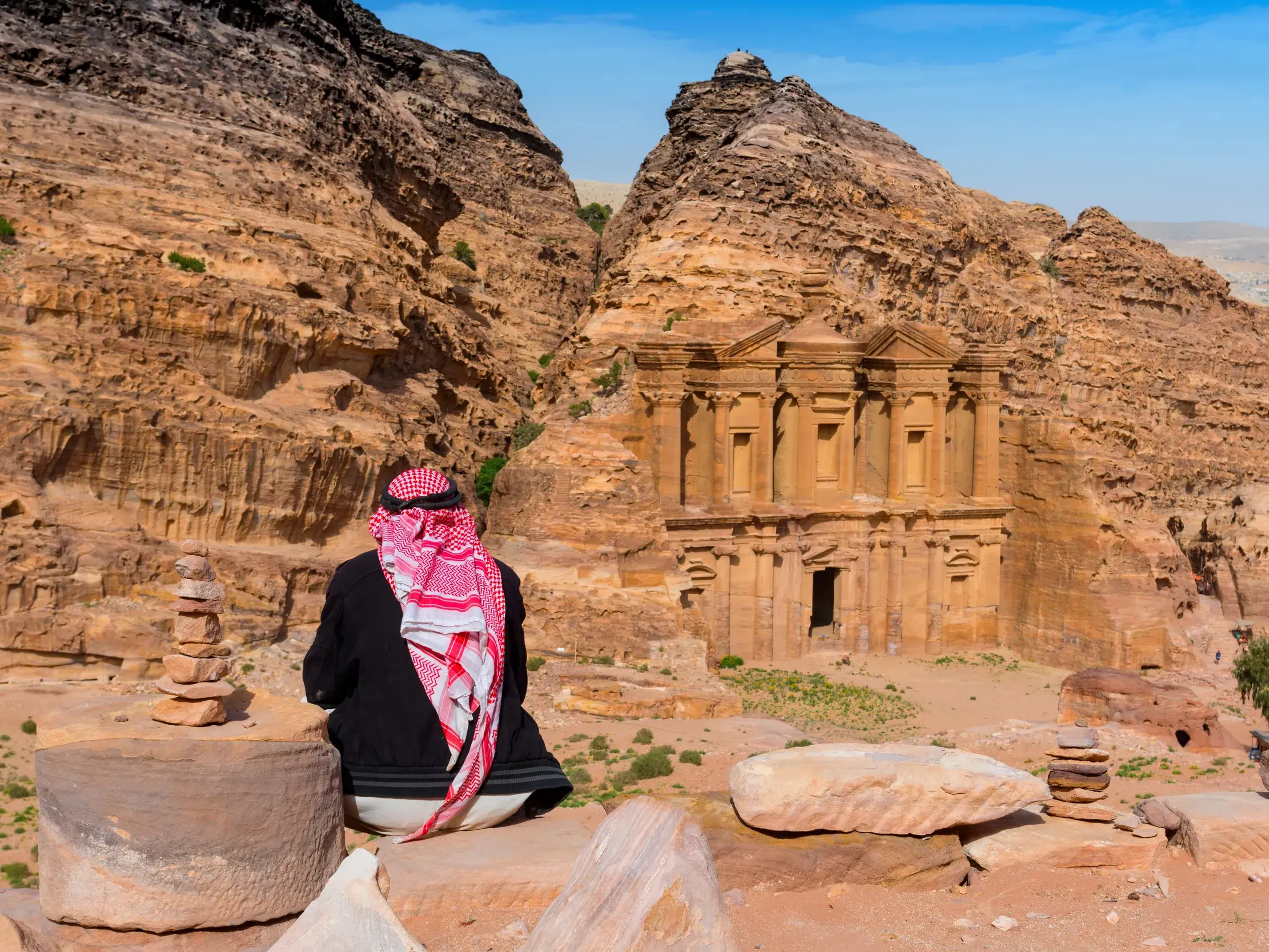 Ein Mann mit traditioneller Kufiya-Kopfbedeckung blickt auf das in den Fels gehauene Kloster Ad-Deir in Petra, Jordanien.
