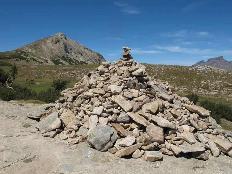 Ein Steinmännchen auf dem GR20 Trekkingpfad in Korsika, im Hintergrund die weite Berglandschaft mit einem markanten Gipfel.