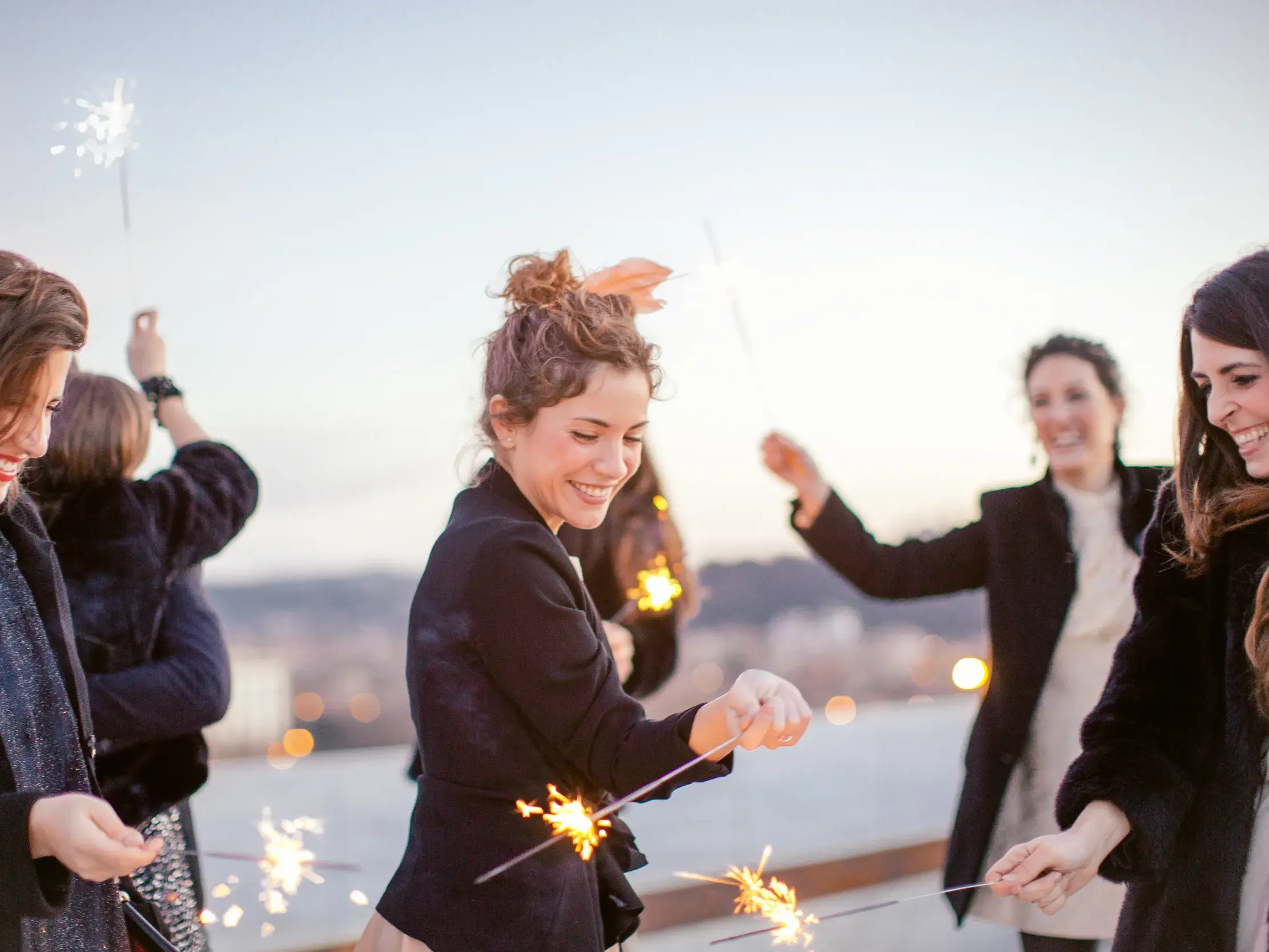 Gruppe von Alleinreisenden feiert lachend mit Wunderkerzen den Jahreswechsel auf einer Silvesterreise in Athen.