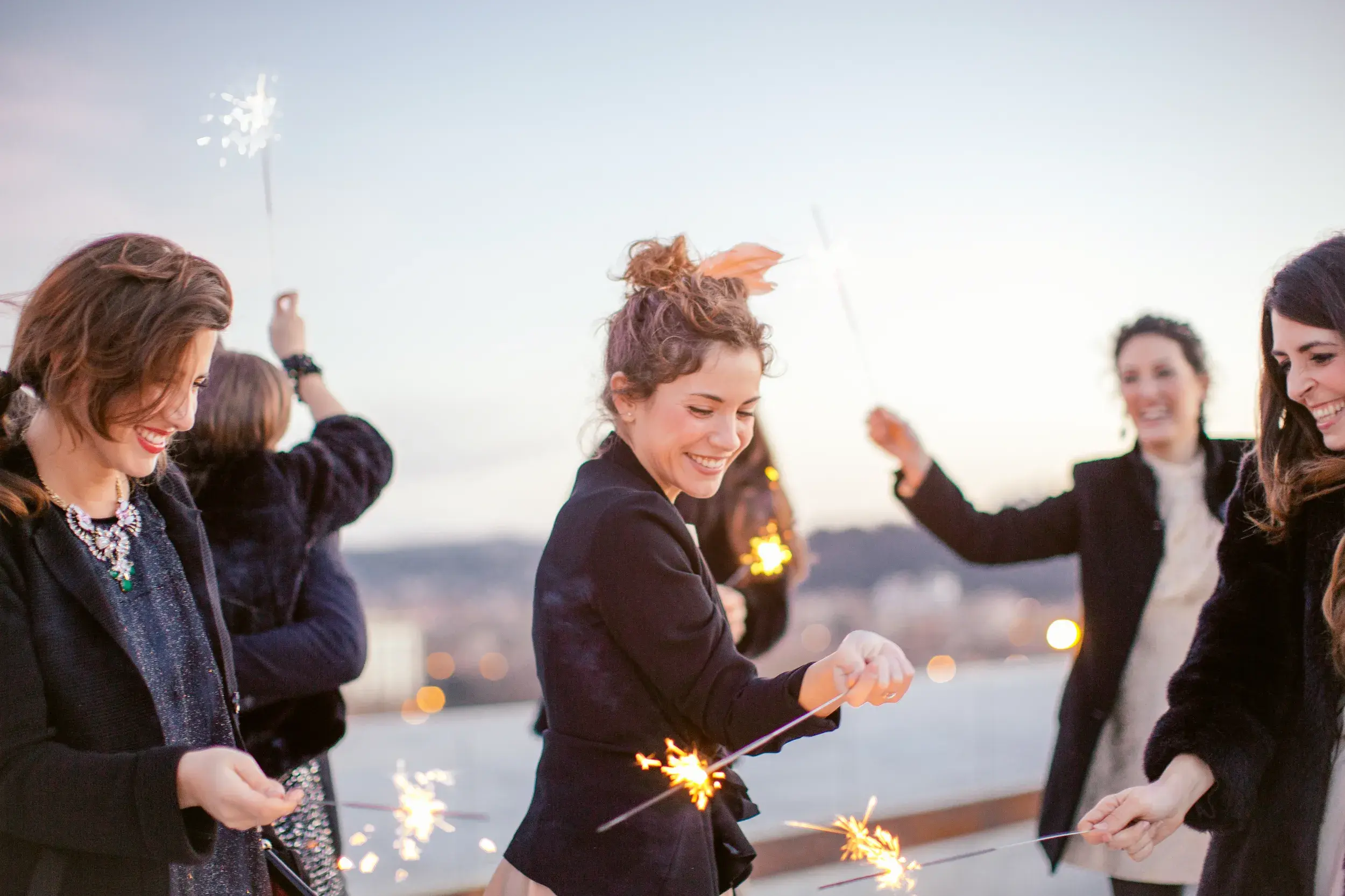 Gruppe von Alleinreisenden feiert lachend mit Wunderkerzen den Jahreswechsel auf einer Silvesterreise in Athen.