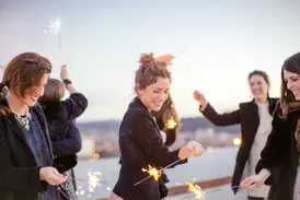 Gruppe von Alleinreisenden feiert lachend mit Wunderkerzen den Jahreswechsel auf einer Silvesterreise in Athen.