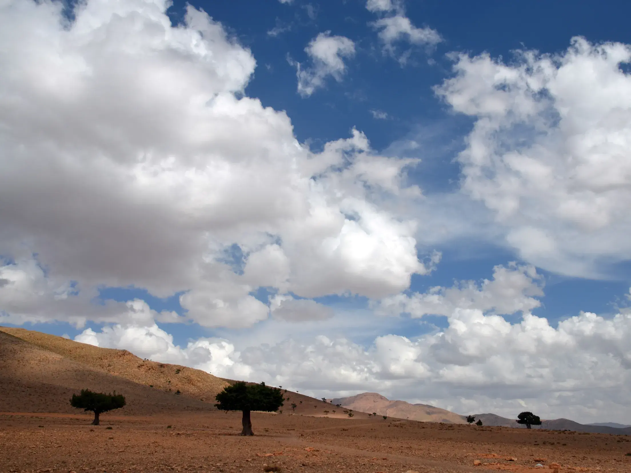 Wanderung durch die aride Hügellandschaft des Atlasgebirges in Marokko unter einem weiten, blauen Wolkenhimmel.