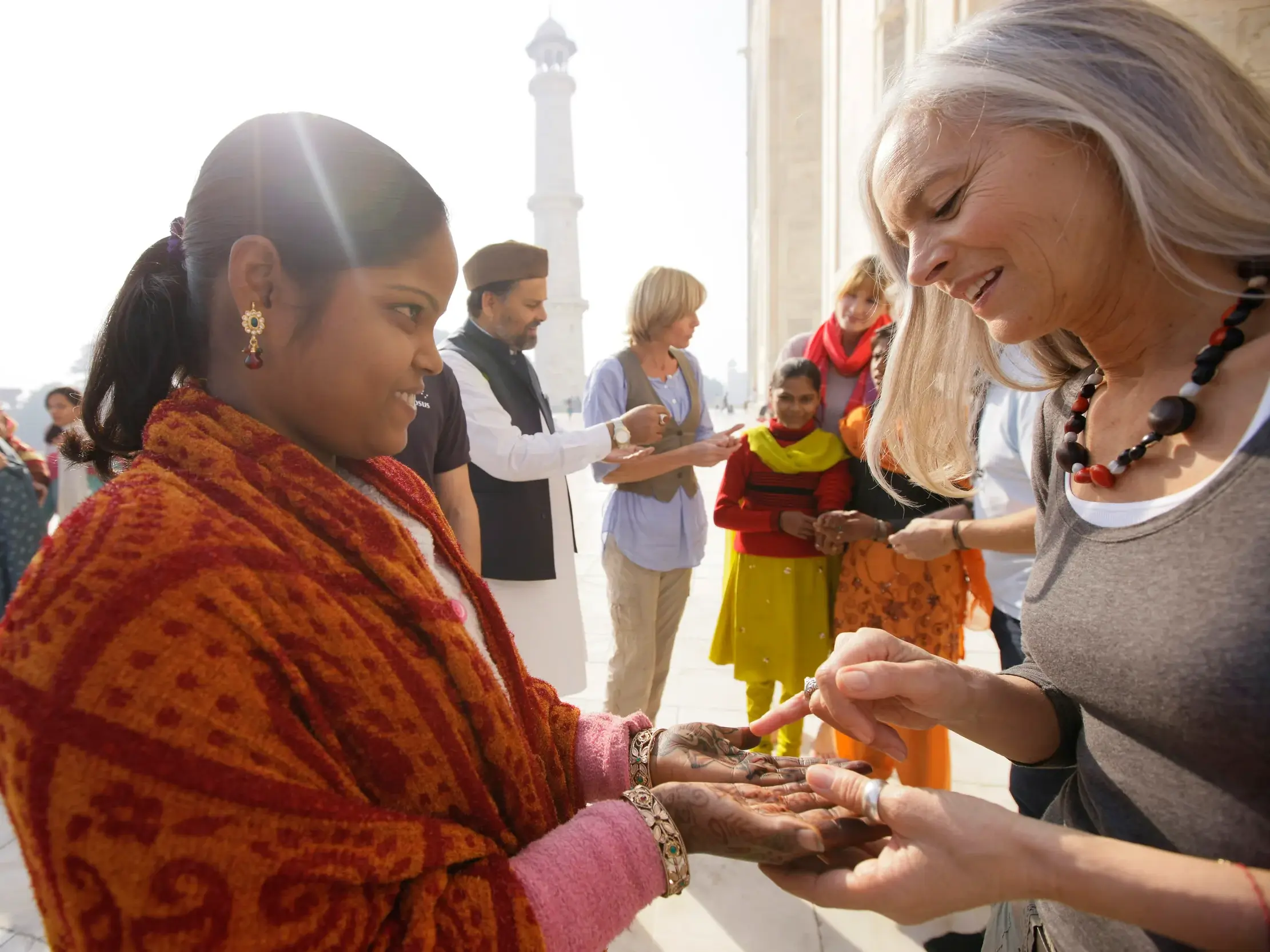 Eine Dame auf einer geführten Gruppenreise bewundert die Henna-Bemalung einer Inderin am Taj Mahal in Agra.