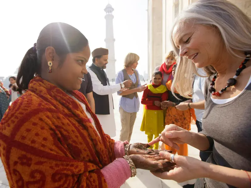 Eine Dame auf einer geführten Gruppenreise bewundert die Henna-Bemalung einer Inderin am Taj Mahal in Agra.
