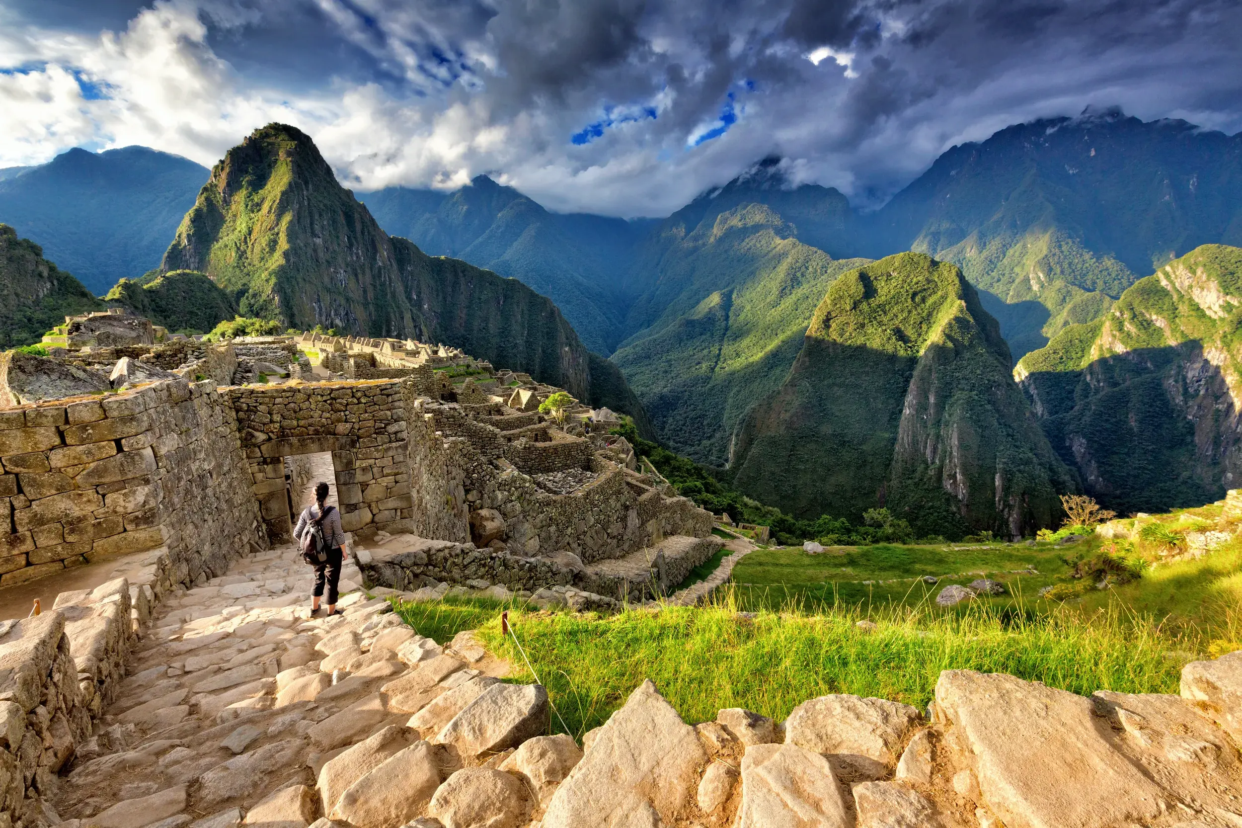 Ein Reisender mit Rucksack erkundet die berühmten Ruinen von Machu Picchu bei dramatischem Himmel in den Anden Perus.