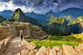 Ein Reisender mit Rucksack erkundet die berühmten Ruinen von Machu Picchu bei dramatischem Himmel in den Anden Perus.
