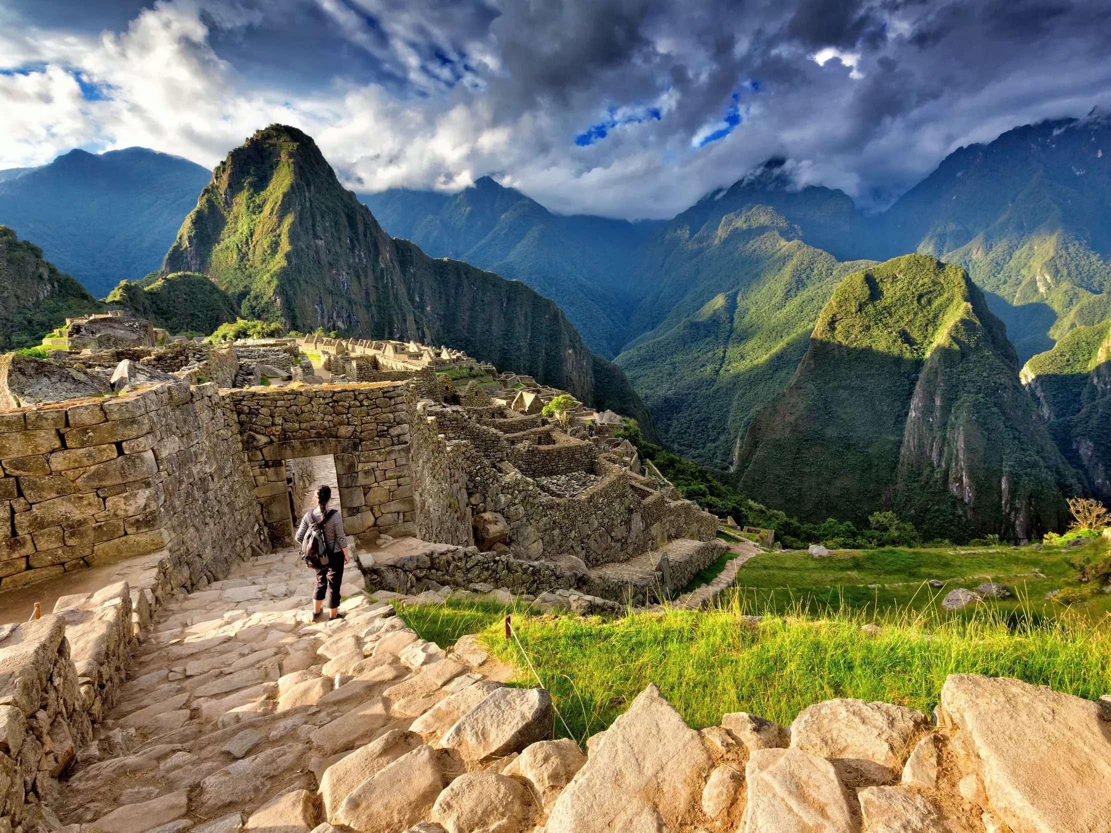 Reisender mit Rucksack auf Steintreppen in der Inkastadt Machu Picchu mit Blick auf die grünen Berggipfel der Anden in Peru.