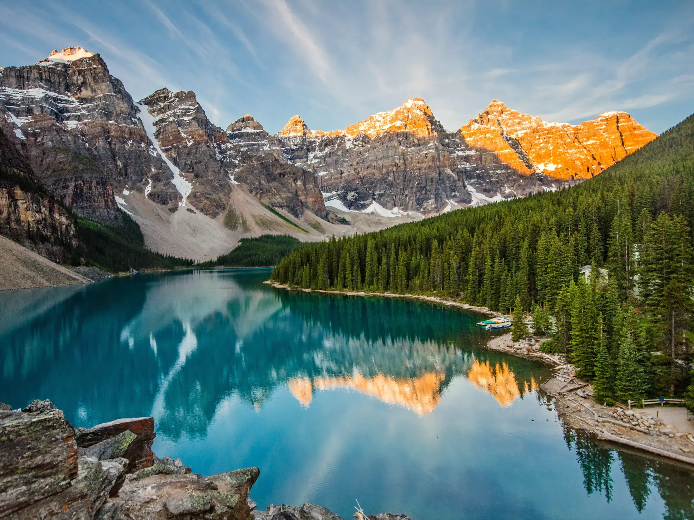 Die Gipfel der Rocky Mountains leuchten im Morgenrot und spiegeln sich im türkisen Moraine Lake im Banff-Nationalpark.