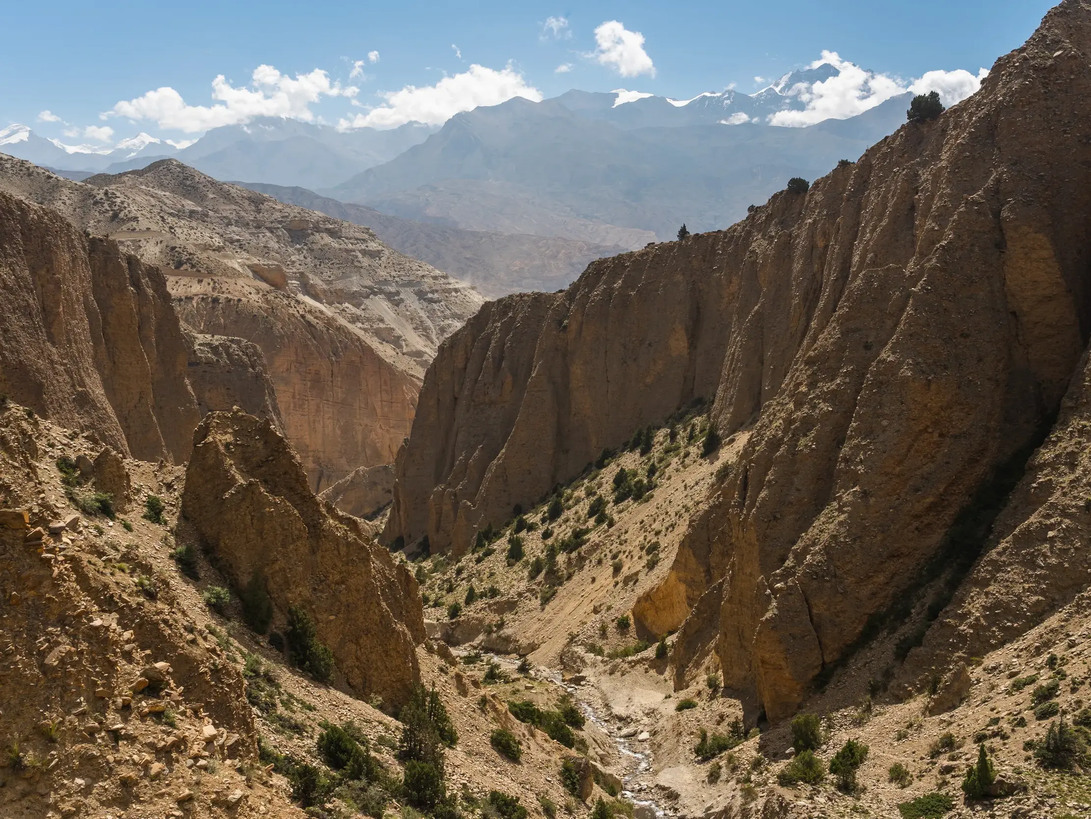Tiefe, ockerfarbene Felsschlucht beim Trekking im ehemaligen Königreich Mustang mit den schneebedeckten Gipfeln des Himalaya.