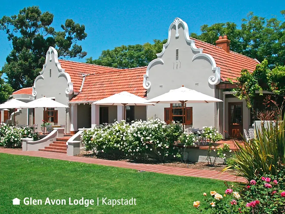 Die Glen Avon Lodge in Constantia bei Kapstadt mit kapholländischem Giebel, umgeben von einem blühenden Garten mit Terrasse.