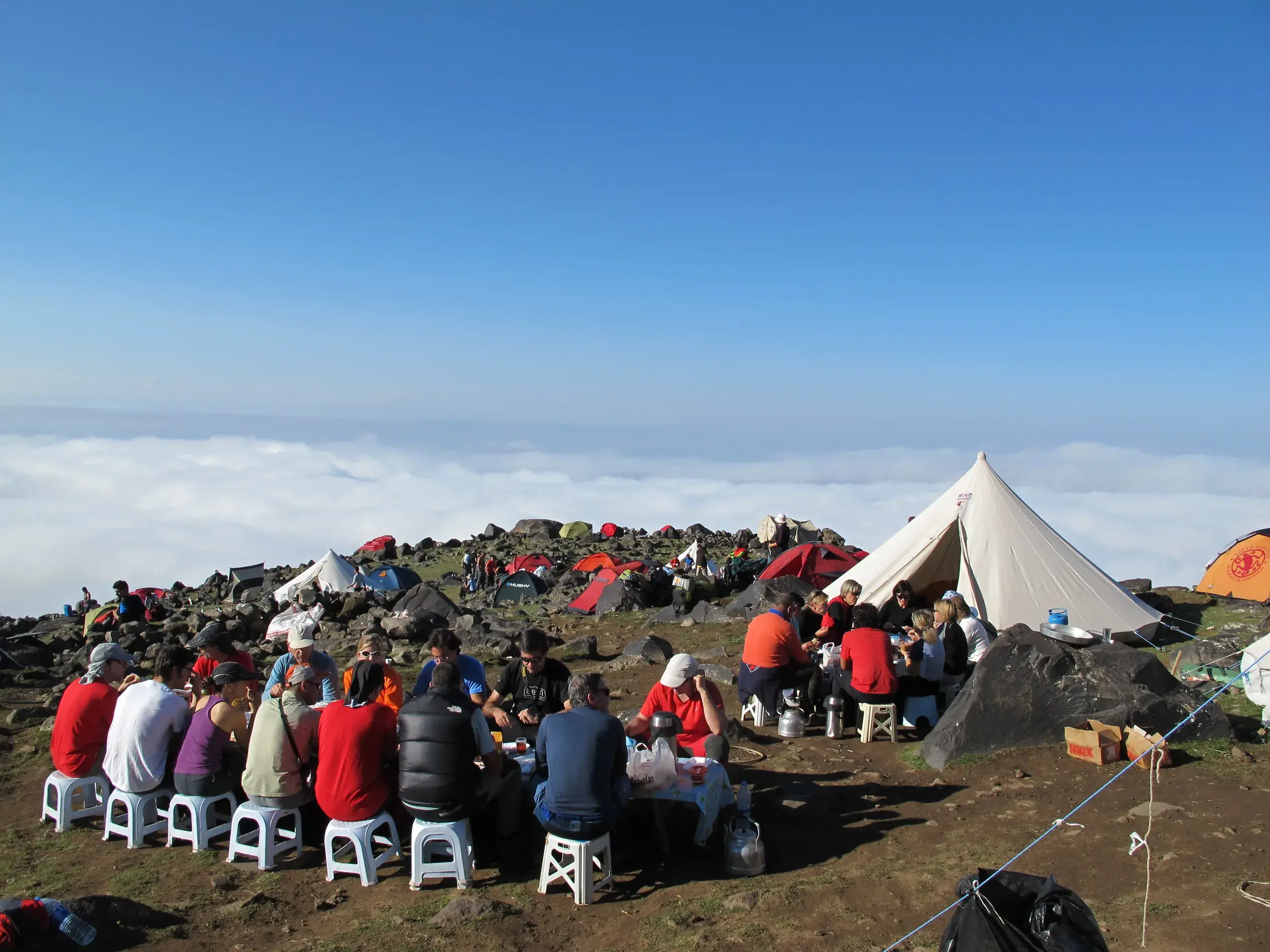 Große Trekking-Gruppe beim gemeinsamen Essen im Basislager am Ararat, umgeben von Zelten und einer dichten Wolkendecke.
