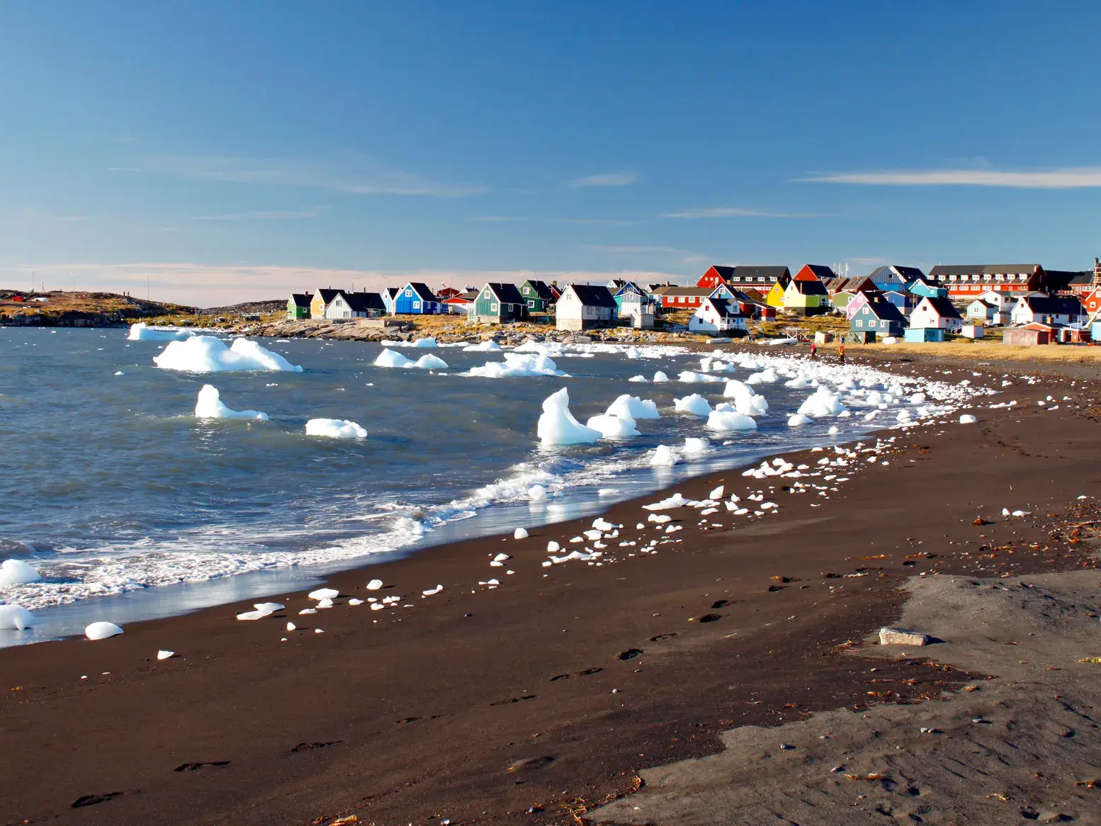 Bunte Holzhäuser in Qeqertarsuaq am dunklen Sandstrand der Diskobucht, an dem kleine Eisberge angespült wurden.