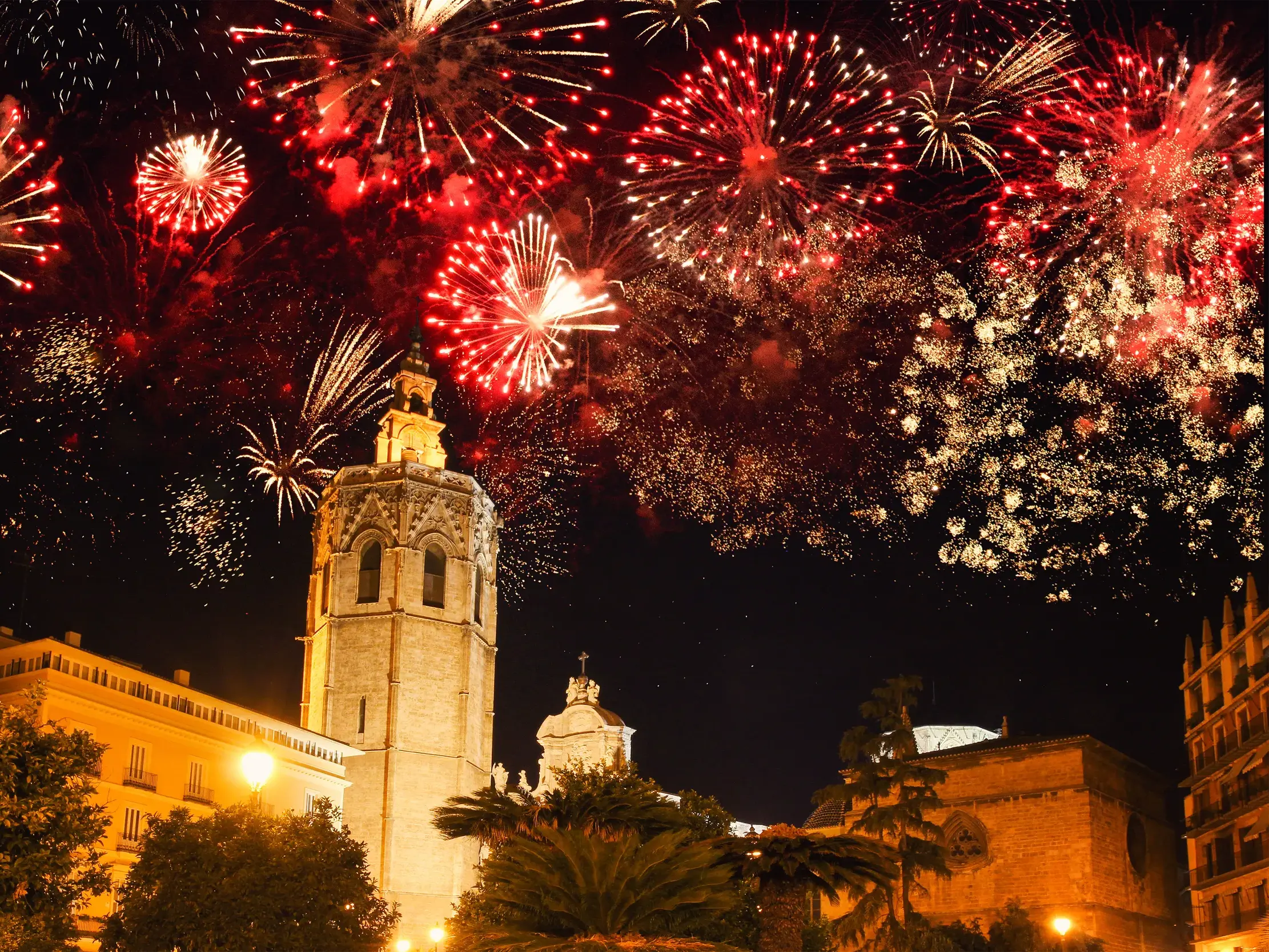 Rotes und goldenes Silvester-Feuerwerk explodiert am Nachthimmel über dem Glockenturm der Kathedrale in der Altstadt von Valencia.