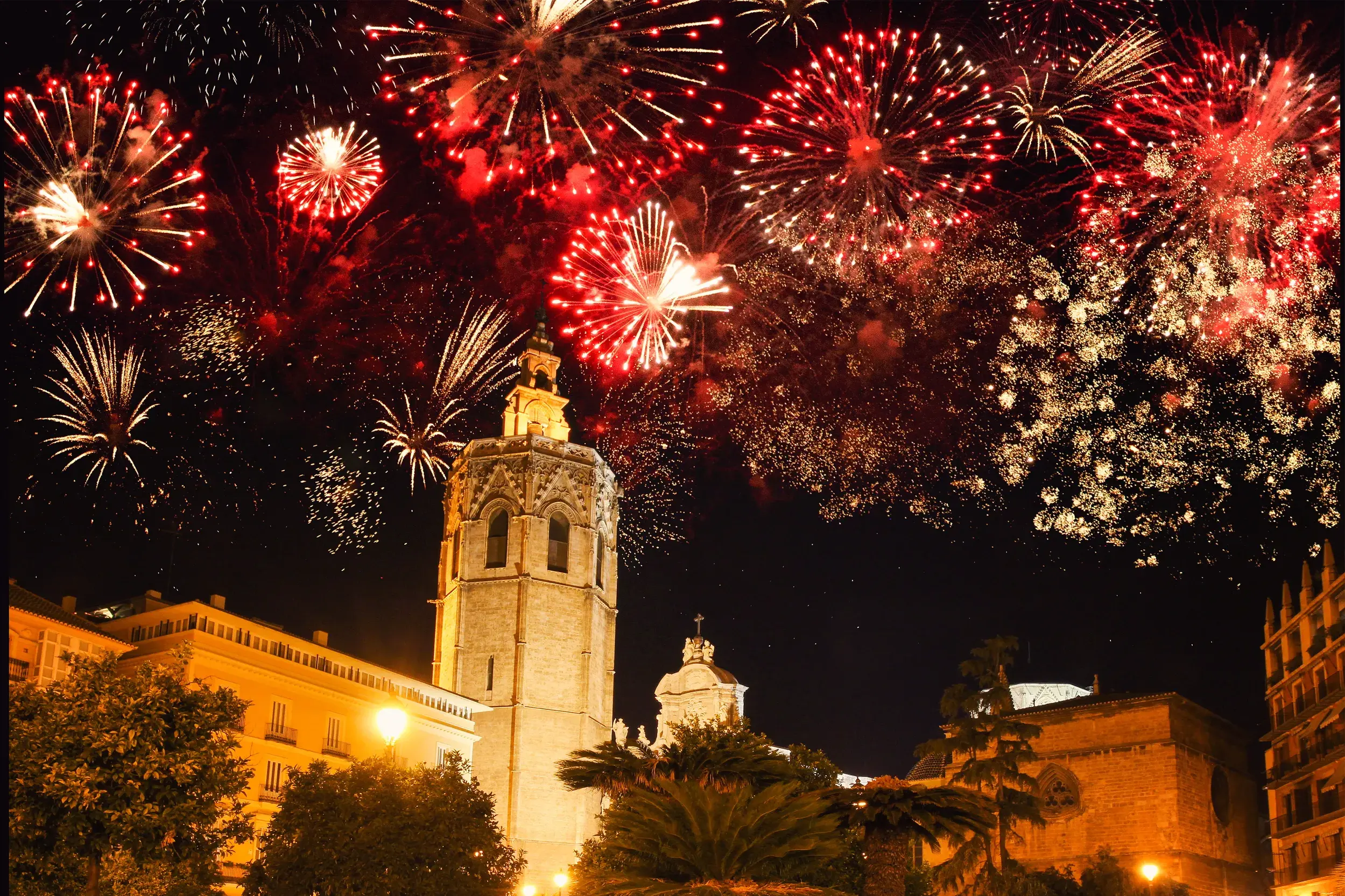 Rotes und goldenes Silvester-Feuerwerk explodiert am Nachthimmel über dem Glockenturm der Kathedrale in der Altstadt von Valencia.