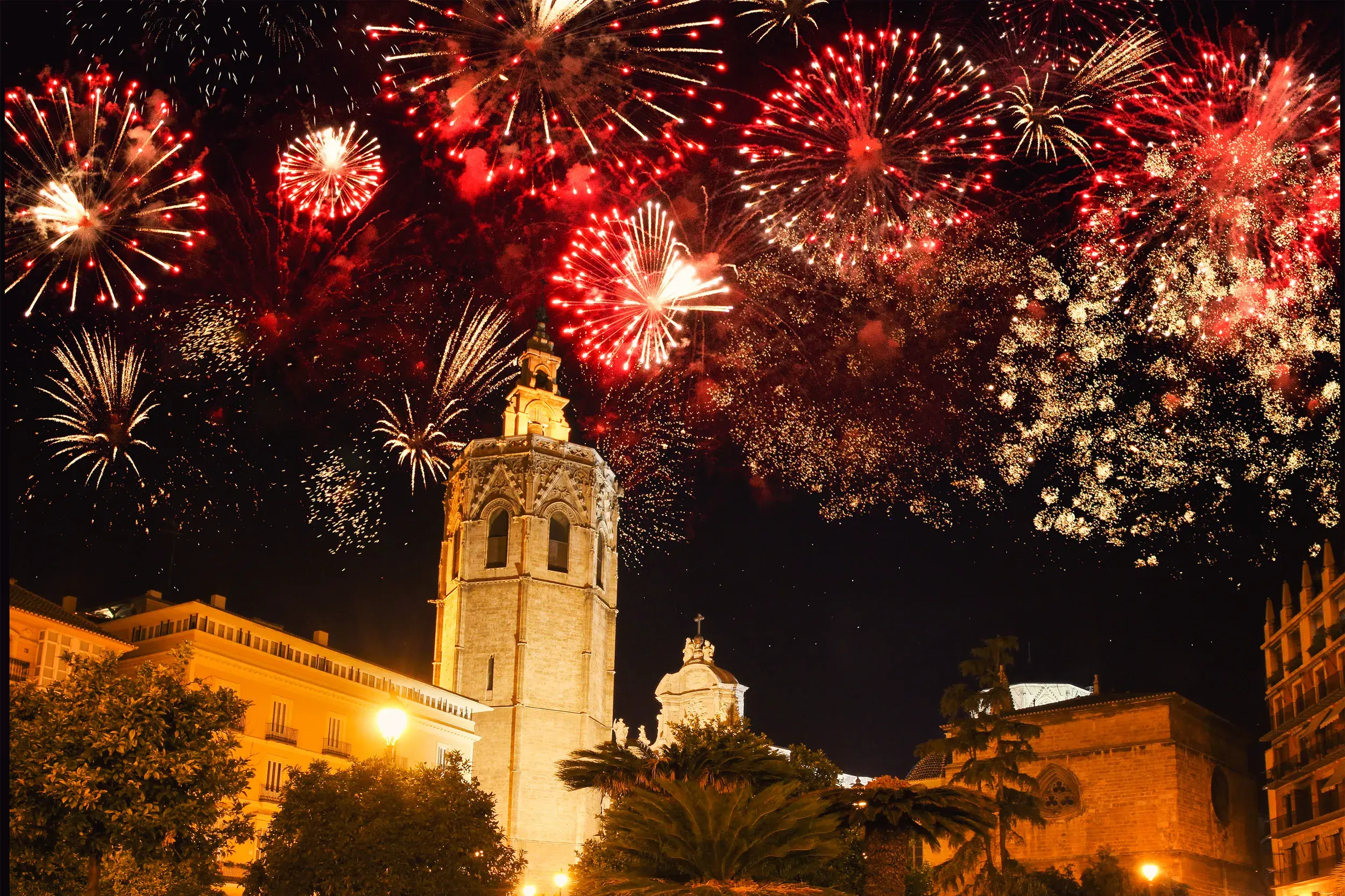 Rotes und goldenes Silvester-Feuerwerk explodiert am Nachthimmel über dem Glockenturm der Kathedrale in der Altstadt von Valencia.