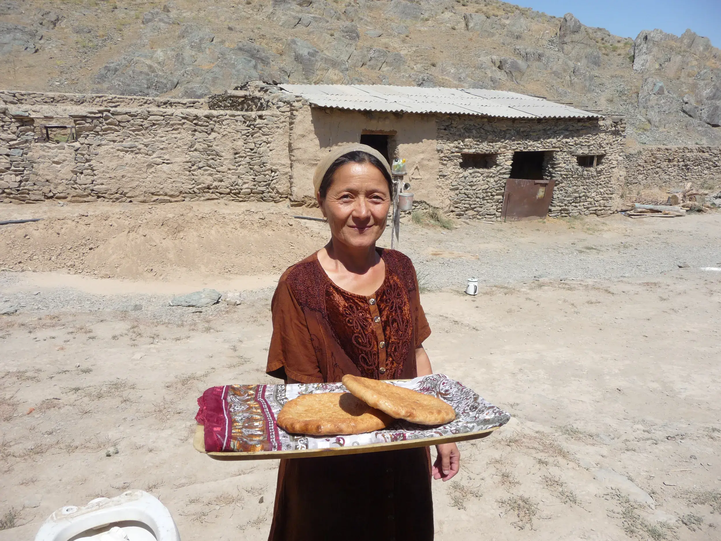Gastgeberin eines Homestays im Nuratau-Gebirge in Usbekistan reicht Reisenden traditionelles, frisches Fladenbrot.