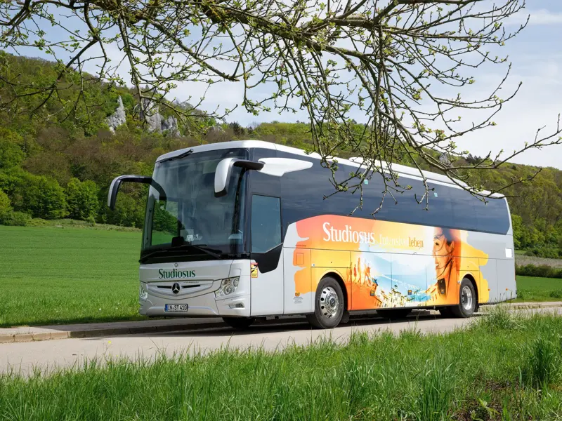 Der Studiosus Komfortbus bei einer Pause auf einer Panoramastraße, umgeben von grünen Wiesen und bewaldeten Hügeln.