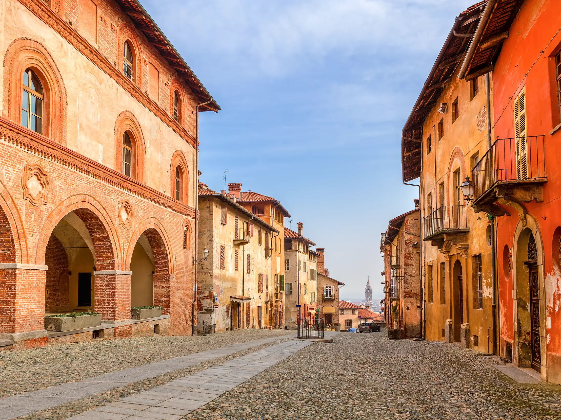 Malerische, kopfsteingepflasterte Altstadtgasse in Saluzzo, Piemont, gesäumt von historischen Gebäuden mit Arkadengängen.