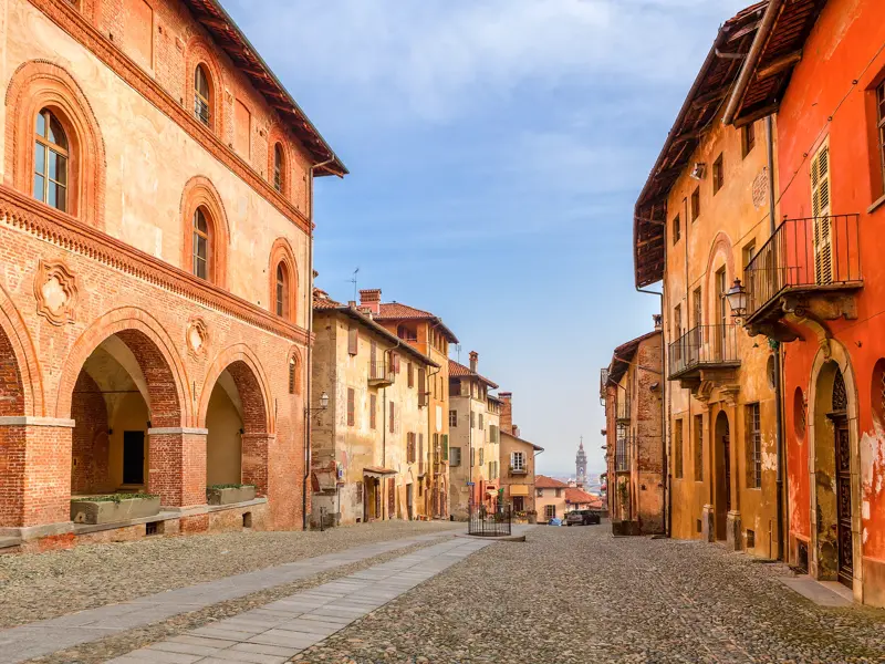 Malerische, kopfsteingepflasterte Altstadtgasse in Saluzzo, Piemont, gesäumt von historischen Gebäuden mit Arkadengängen.