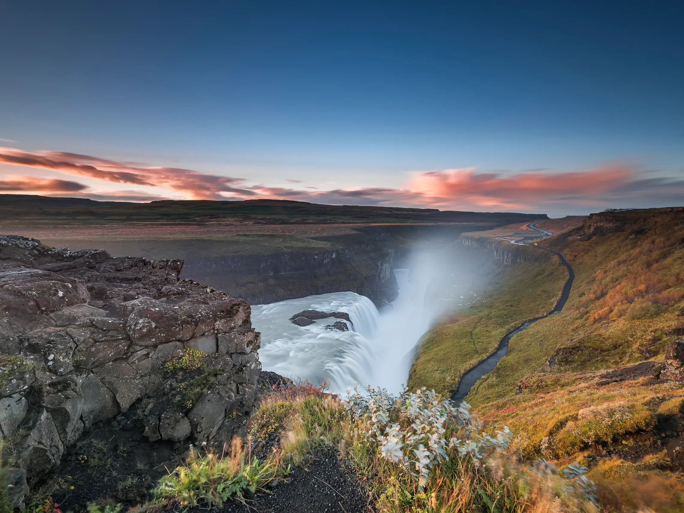 Der Gullfoss Wasserfall in Island, Teil des Goldenen Rings, stürzt bei Abendrot in eine weite, moosbewachsene Schlucht.