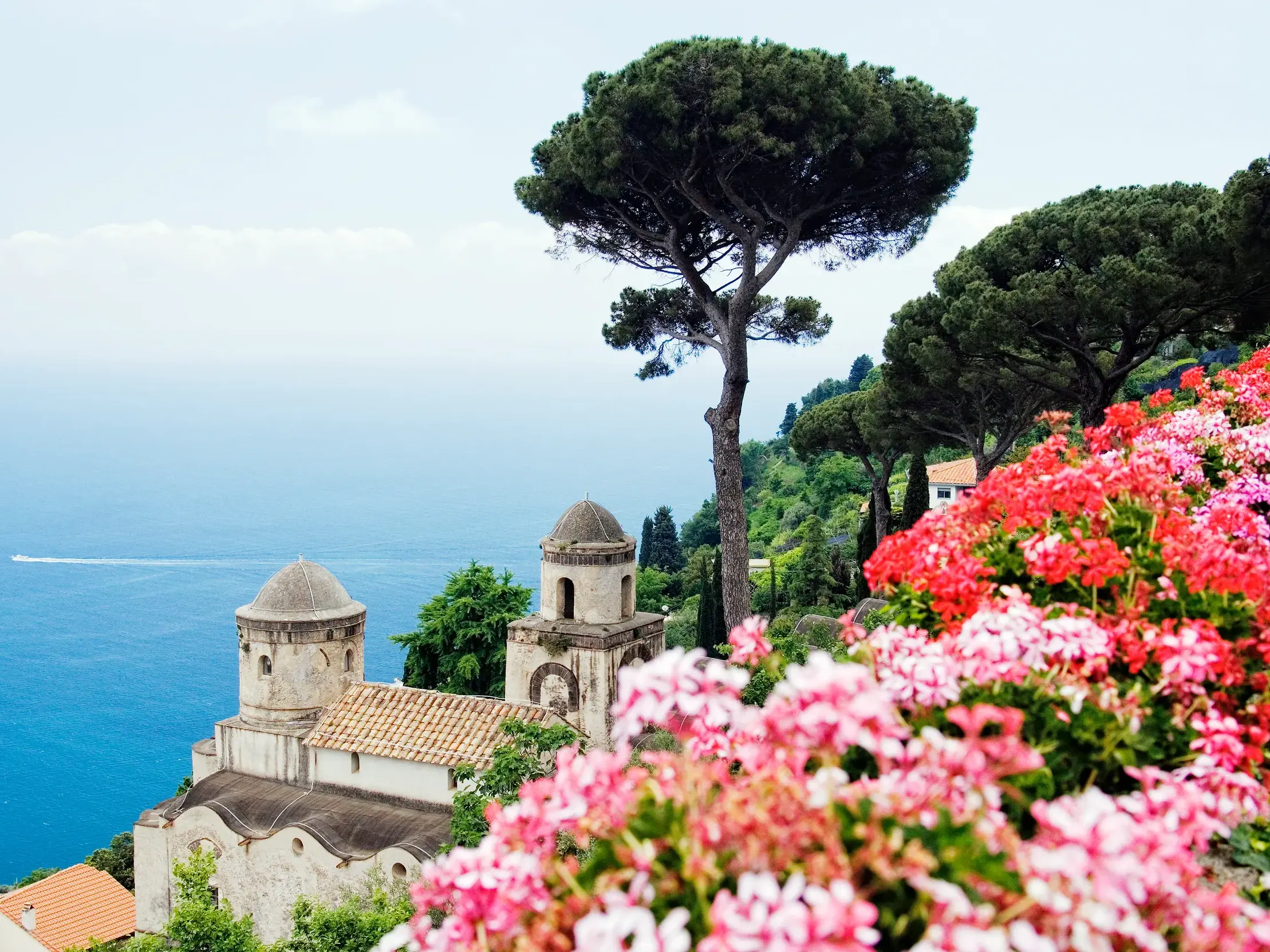 Blick von den Gärten der Villa Rufolo in Ravello über eine Pinie und eine Kirche auf das tiefblaue Meer der Amalfiküste.