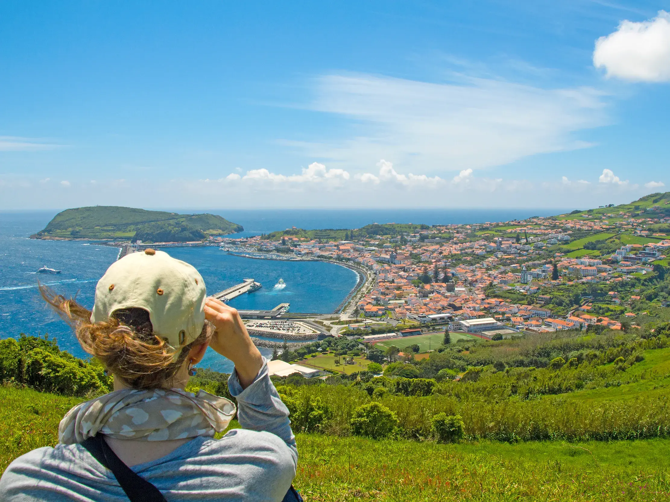 Reisende genießt von grünen Hügeln den Panoramablick auf die Hafenstadt Horta und den Atlantik auf der Azoren-Insel Faial.