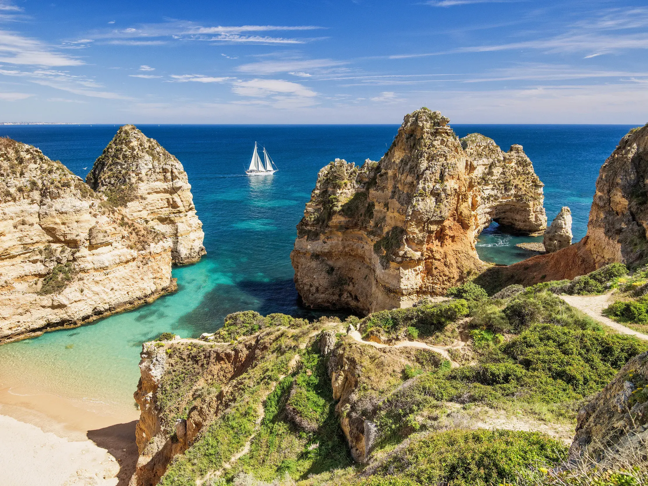 Wanderweg auf den Klippen der Ponta da Piedade mit Blick auf die Felsküste der Algarve und ein Segelboot auf dem Atlantik.