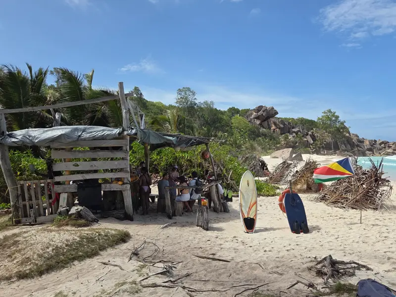 Wandergruppe bei einer Pause an einer improvisierten Strandbar mit Seychellen-Flagge am Strand Anse Coco auf La Digue.