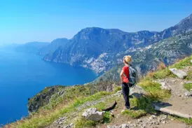 Eine Wanderin pausiert auf dem Sentiero degli Dei und blickt auf die steilen Klippen und das blaue Meer der Amalfiküste.
