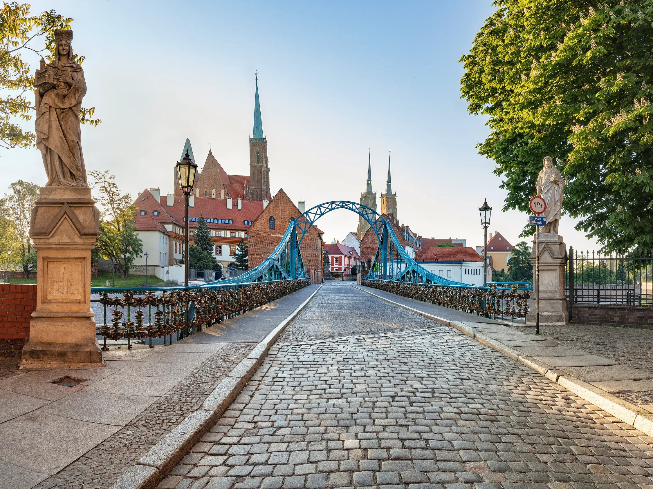 Die kopfsteingepflasterte Most Tumski Brücke, gesäumt von Statuen, führt in Breslau bei Sonnenschein zur Dominsel.