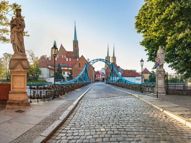 Die kopfsteingepflasterte Most Tumski Brücke, gesäumt von Statuen, führt in Breslau bei Sonnenschein zur Dominsel.